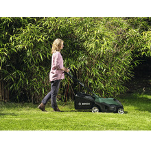 Femme utilisant une tondeuse à gazon dans un jardin devant une haie de bambous