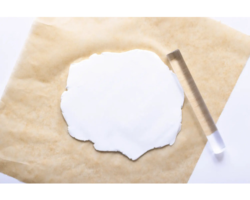 Ein Stück weiße Modelliermasse auf einem Backpapier mit einer Acrylrolle.