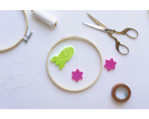 Bastelszene mit Stickrahmen, Rakete, Sternen, Schere und Klebeband