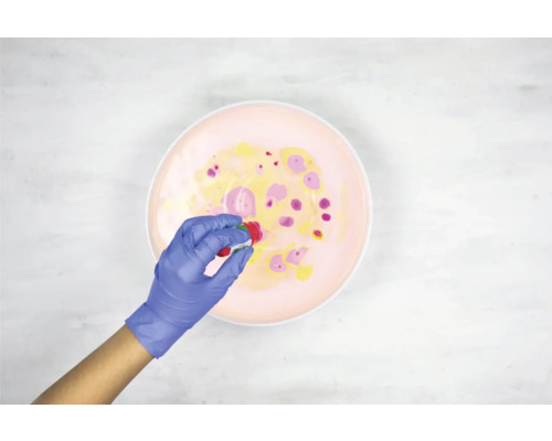 Une personne portant des gants ajoute de la peinture dans un récipient pour créer un effet marbré.