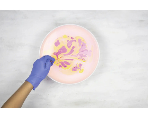 Personne avec des gants marbrant des couleurs dans un bol.