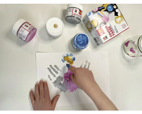 Kind malt mit Fingerfarben auf Papier, verschiedene Farbtöpfe und ein Glas stehen bereit