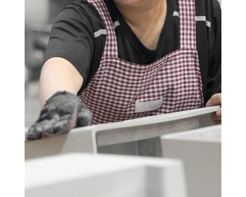 Eine Person mit Schürze und Handschuh berührt ein Produkt.