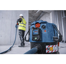 Aspirateur industriel avec tuyau et ouvrier du bâtiment en arrière-plan