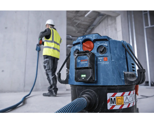 Aspirateur industriel avec tuyau et ouvrier du bâtiment en arrière-plan