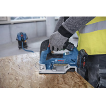 Une personne scie un trou dans une planche de bois avec une scie sauteuse. Un aspirateur est visible à l''arrière-plan.