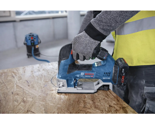 Une personne scie un trou dans une planche de bois avec une scie sauteuse. Un aspirateur est visible à l''arrière-plan.