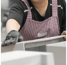 Eine Person mit Handschuhen und einer Schürze untersucht ein Produkt.