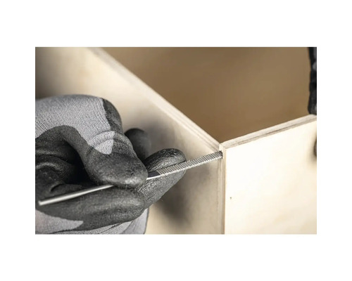 Une personne lime une caisse en bois avec une lime à aiguille.