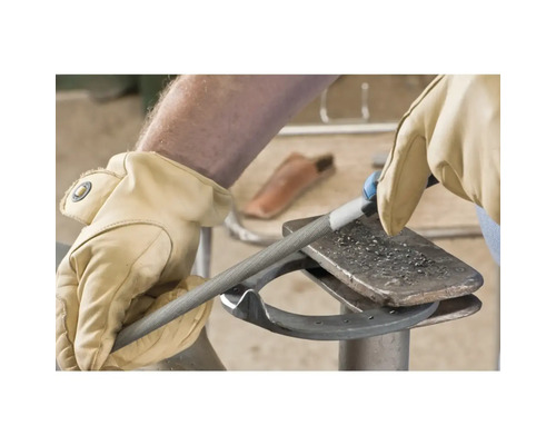 Eine Person feilt mit einer Rundfeile Metall auf einem Amboss, getragen werden Arbeitshandschuhe.