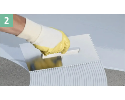 Une personne appliquant de la colle avec une spatule crantée.