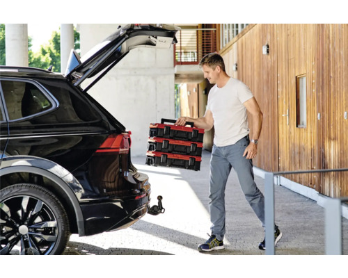 Un homme décharge des boîtes à outils rouges d''une voiture noire