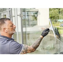 Mann reinigt Fenster mit einem Fensterabzieher