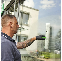 Ein Mann reinigt mit einem Fensterwischer eine Fensterscheibe.