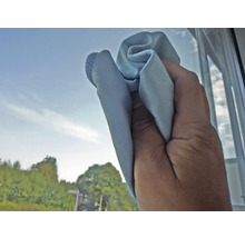 Eine Hand wischt mit einem Reinigungstuch über eine Fensterscheibe