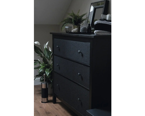 Commode sombre avec trois tiroirs, miroir, plante et décoration dans une chambre.