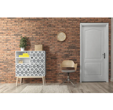 Salon avec commode, chaise et porte devant un mur en briques.