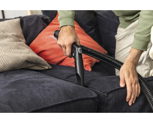 Person reinigt Sofa mit Staubsaugerdüse