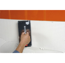 Application d''une spatule crantée pour appliquer de la colle sur un mur sous des carreaux