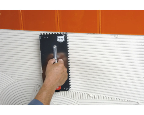 Application d''une spatule crantée pour appliquer de la colle sur un mur sous des carreaux