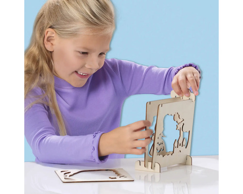 Ein Mädchen montiert ein hölzernes Fensterbild mit Märchenmotiven.