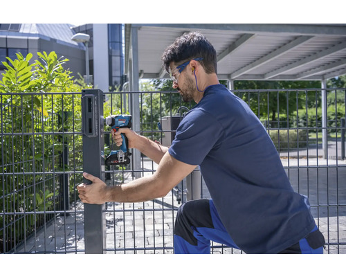 Un homme monte un poteau de clôture avec une visseuse sans fil.