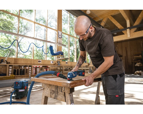 Un artisan utilise une ponceuse multifonction pour poncer un cadre en bois avec aspiration de poussière dans un atelier.