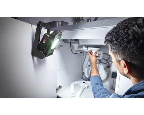 Un homme répare la canalisation sous l'évier avec une lampe Bosch
