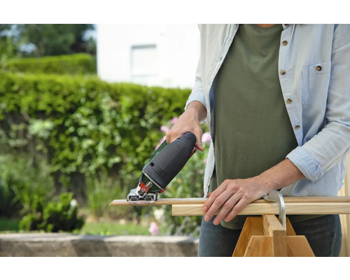 Une femme coupe une planche de bois à l'extérieur avec une scie sauteuse.