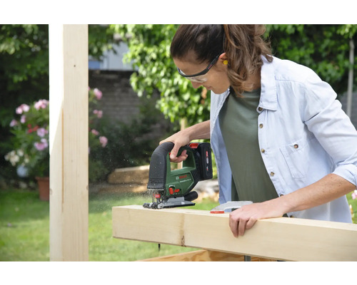 Une femme scie une planche de bois avec une scie sauteuse dans le jardin.