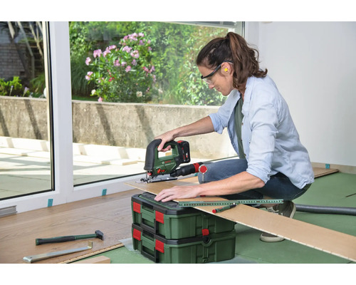 Femme coupant du stratifié avec une scie sauteuse, portant des lunettes de protection et des protections auditives, pose de stratifié sur le sol