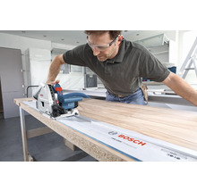 Mann sägt Holzbrett mit einer Bosch Tauchsäge auf einer Führungsschiene.