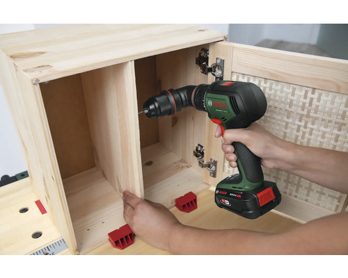 Une personne visse un meuble en bois avec une visseuse sans fil.