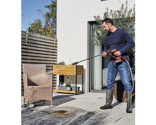 Ein Mann reinigt mit einem Hochdruckreiniger eine Terrasse im Aussenbereich.
