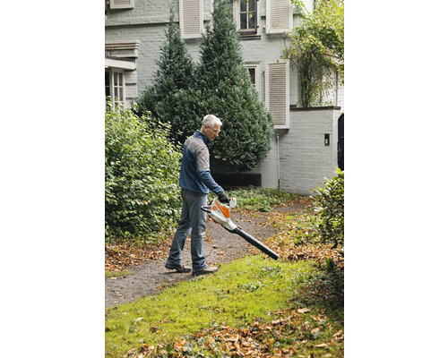 Ein Mann benutzt einen Laubbläser im Garten, um Blätter zu entfernen.