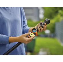 Eine Person hält einen Gartenschlauch mit Sprühkopf und Zubehör in der Hand.