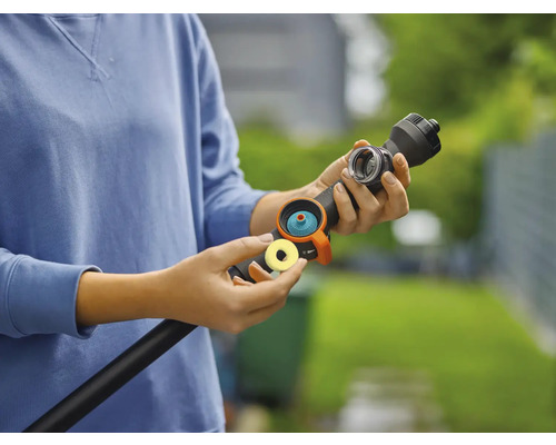 Une personne tient un tuyau d''arrosage avec embout et accessoires dans sa main.