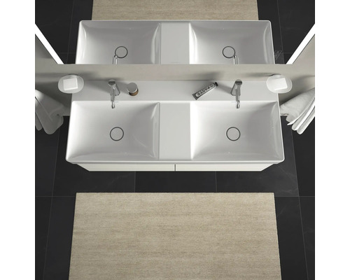 Aufsicht auf ein Doppelwaschbecken mit Armaturen, Seifenschalen, Handtüchern und einem Teppich im Badezimmer.