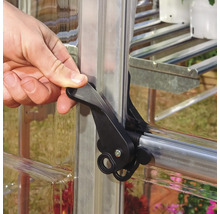 Une main actionne un loquet de fermeture noir sur une fenêtre de serre.