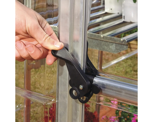 Une main actionne un loquet de fermeture noir sur une fenêtre de serre.