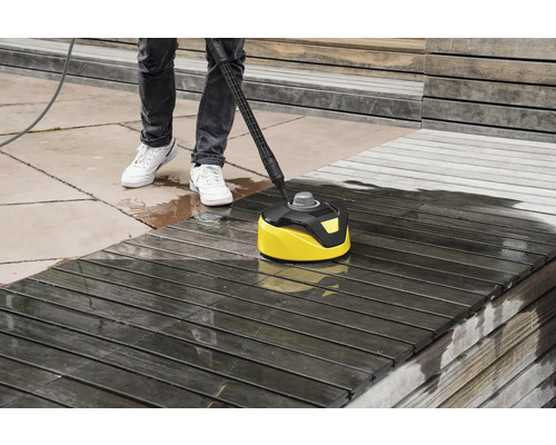 Eine Person reinigt eine Holzterrasse mit einem Flächenreiniger.