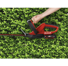 Bedienung einer Einhell Akku-Heckenschere vor einer grünen Hecke