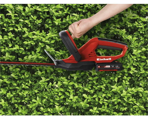 Bedienung einer Einhell Akku-Heckenschere vor einer grünen Hecke