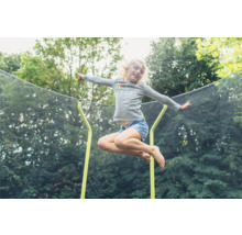 Une fille saute sur un trampoline de jardin avec filet de sécurité.
