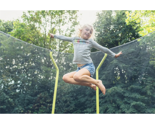 Une fille saute sur un trampoline de jardin avec filet de sécurité.