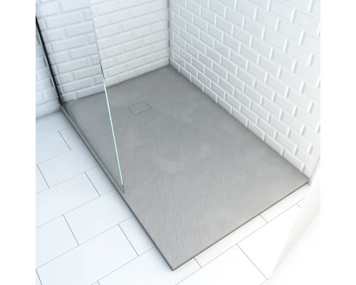 Receveur de douche plat avec drain rectangulaire et paroi de douche en verre dans une salle de bain avec carrelage blanc.