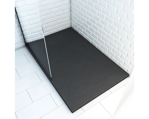 Douche plain-pied avec receveur rectangulaire foncé et paroi de douche en verre devant un mur carrelé blanc.