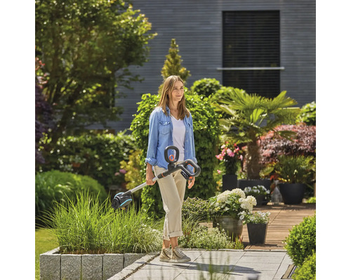 Eine Frau steht mit einem Rasentrimmer in einem Garten.