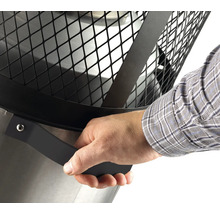 Detailansicht einer Feuerstelle mit Hand am Griff des Schutzgitters.