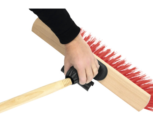 Eine Hand hält eine Kehrbürste mit Holzstiel und roten Borsten.